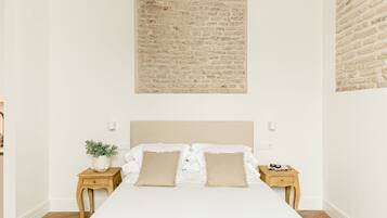 Une chambre avec un grand lit, deux tables de chevet, un mur décoré d’un motif en briques et une petite plante en pot.