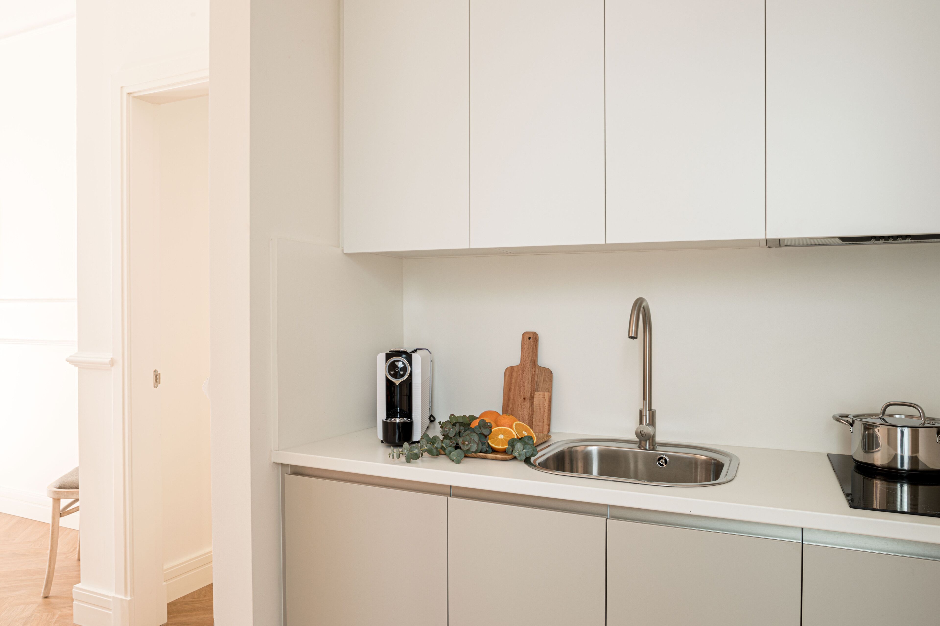 A modern kitchen with white cabinets, a stainless steel sink, a coffee maker, and a cutting board.
