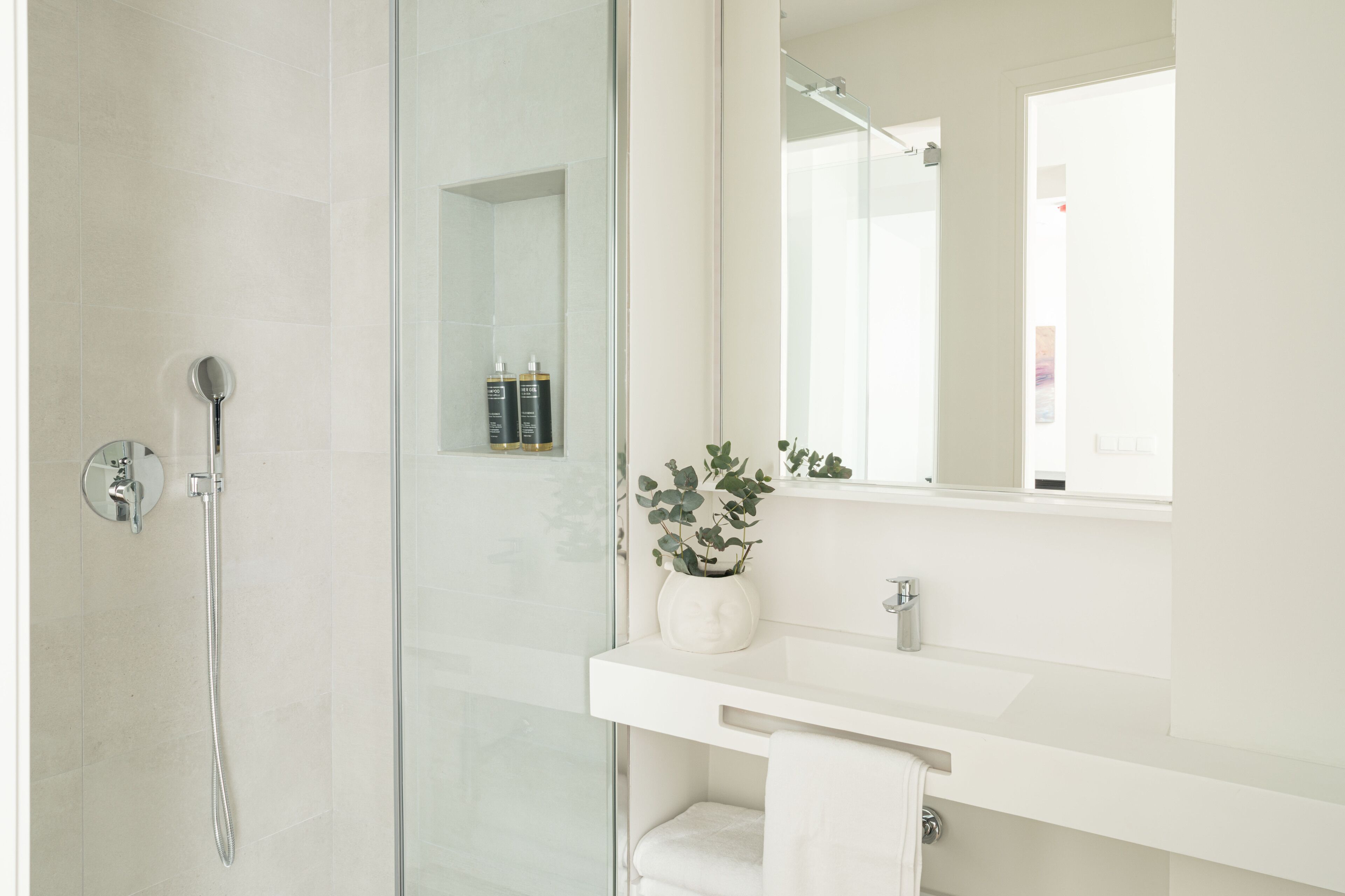 Un bagno moderno con box doccia in vetro, un mobile lavabo bianco con specchio e una pianta in vaso.