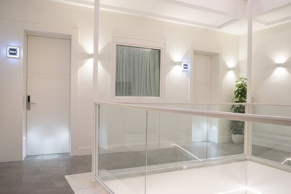 A modern hotel hallway with glass railings, a door with a light switch, and a potted plant. - MYLU SUITES by PUERTA CATEDRAL (Seville)