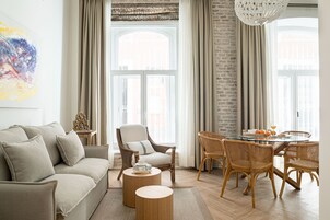 Una sala de estar moderna con sofá, sillones, una mesa de comedor con sillas y un gran ventanal con cortinas.