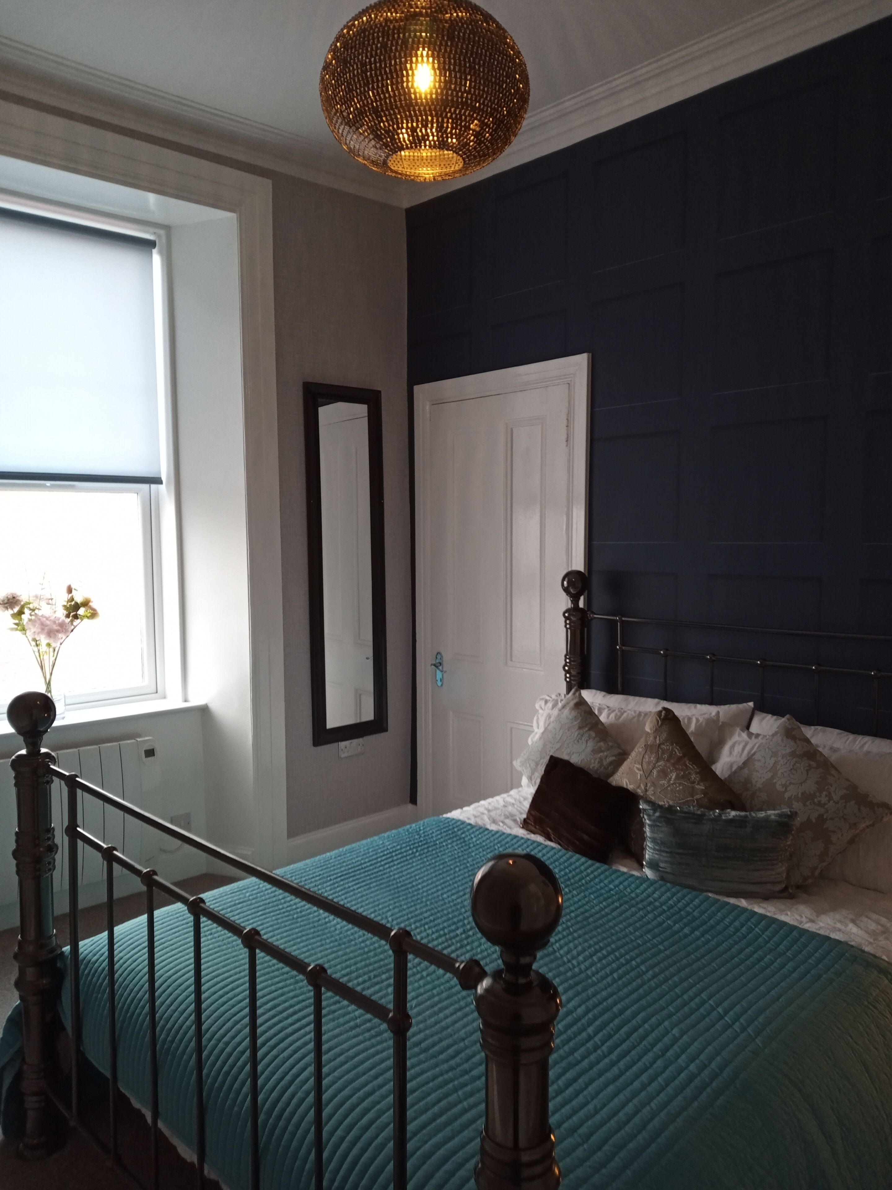 A bedroom with a bed, a window with a view, a door, and a ceiling light fixture.