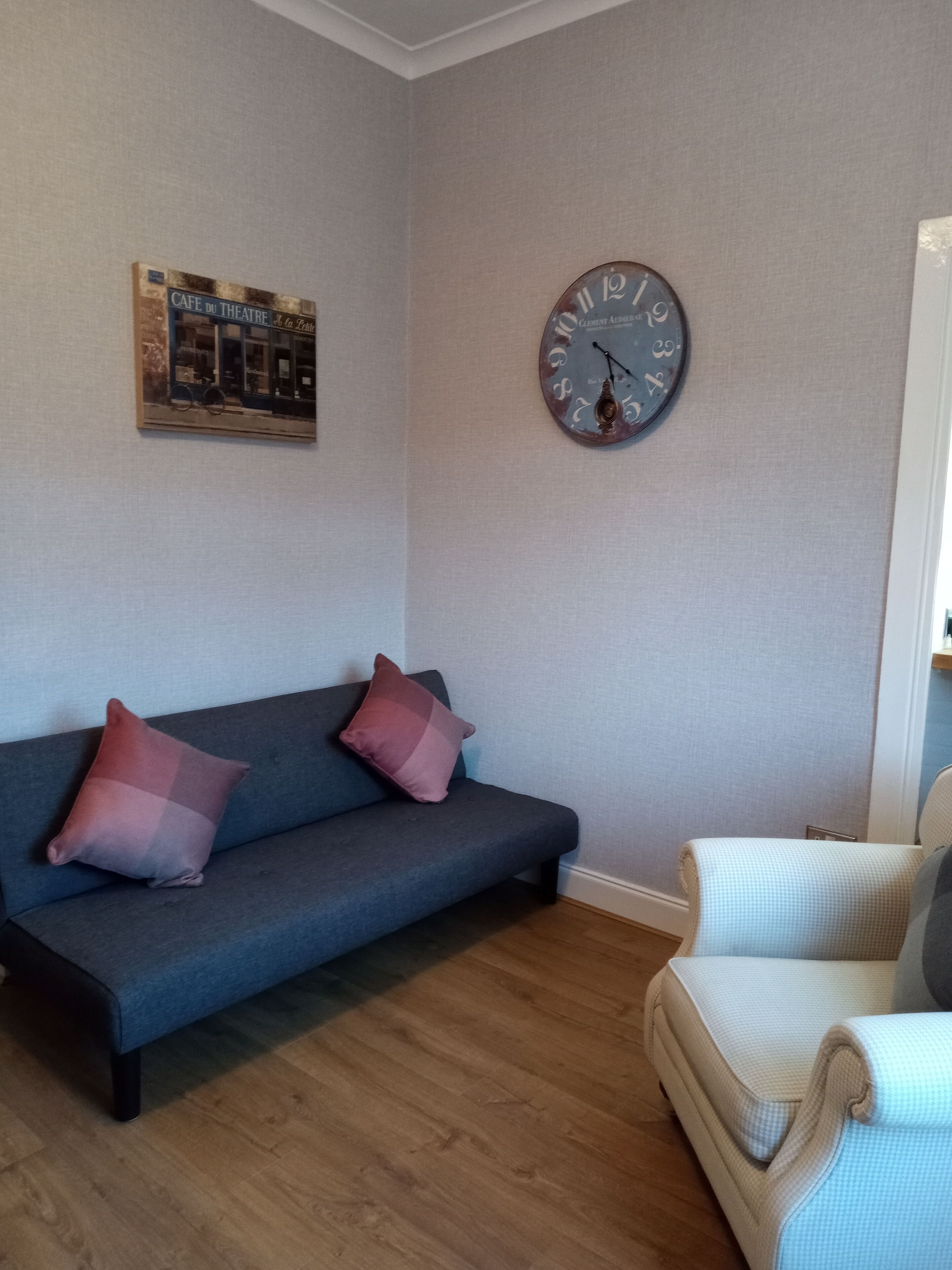 A living room with a blue sofa, two pink cushions, a round wall clock, and a poster on the wall.