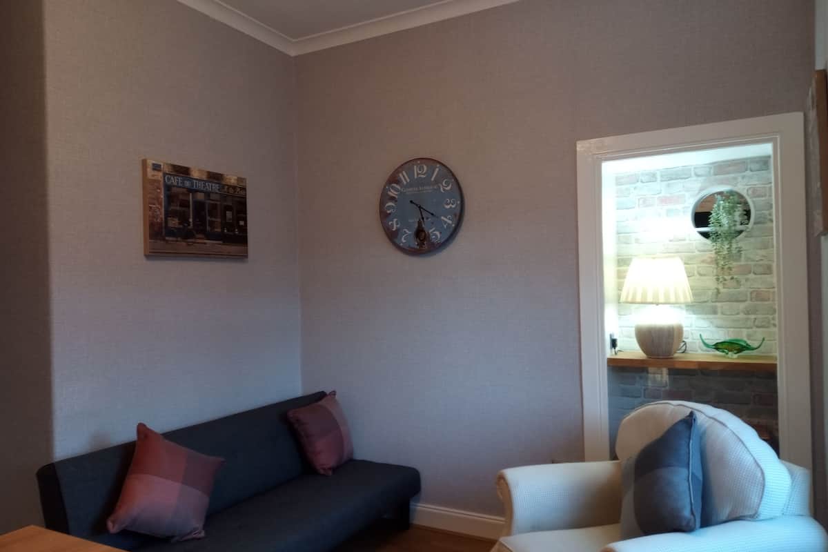 Ein Wohnzimmer mit einem dunkelblauen Sofa, einem weißen Sessel, einer runden Wanduhr und einem gerahmten Bild an der Wand.