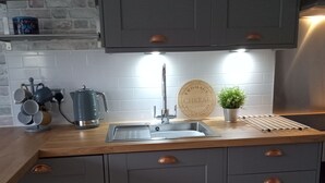 Eine moderne Küche mit grauen Schränken, einer Holz Arbeitsplatte, einer Edelstahl-Spüle und einer Kaffeemaschine.