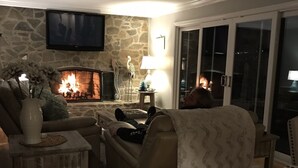 A cozy living room with a stone fireplace, comfortable seating, and a television mounted on the wall.