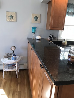 A kitchen with wooden cabinets, a black countertop, a small white table with a decorative item, and wall decorations including a star and a shell.