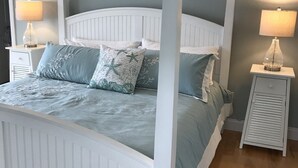 A bedroom with a white four-poster bed, two bedside tables with lamps, and a wooden floor.