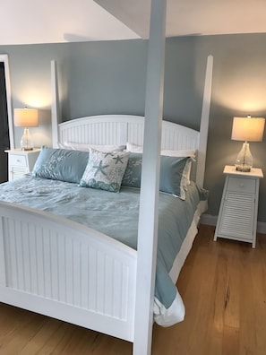 A bedroom with a white four-poster bed, two bedside tables with lamps, and a wooden floor.