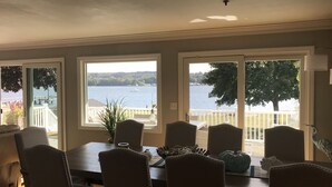 A dining area with a view of a lake and dock, featuring a wooden table, chairs, and a potted plant.