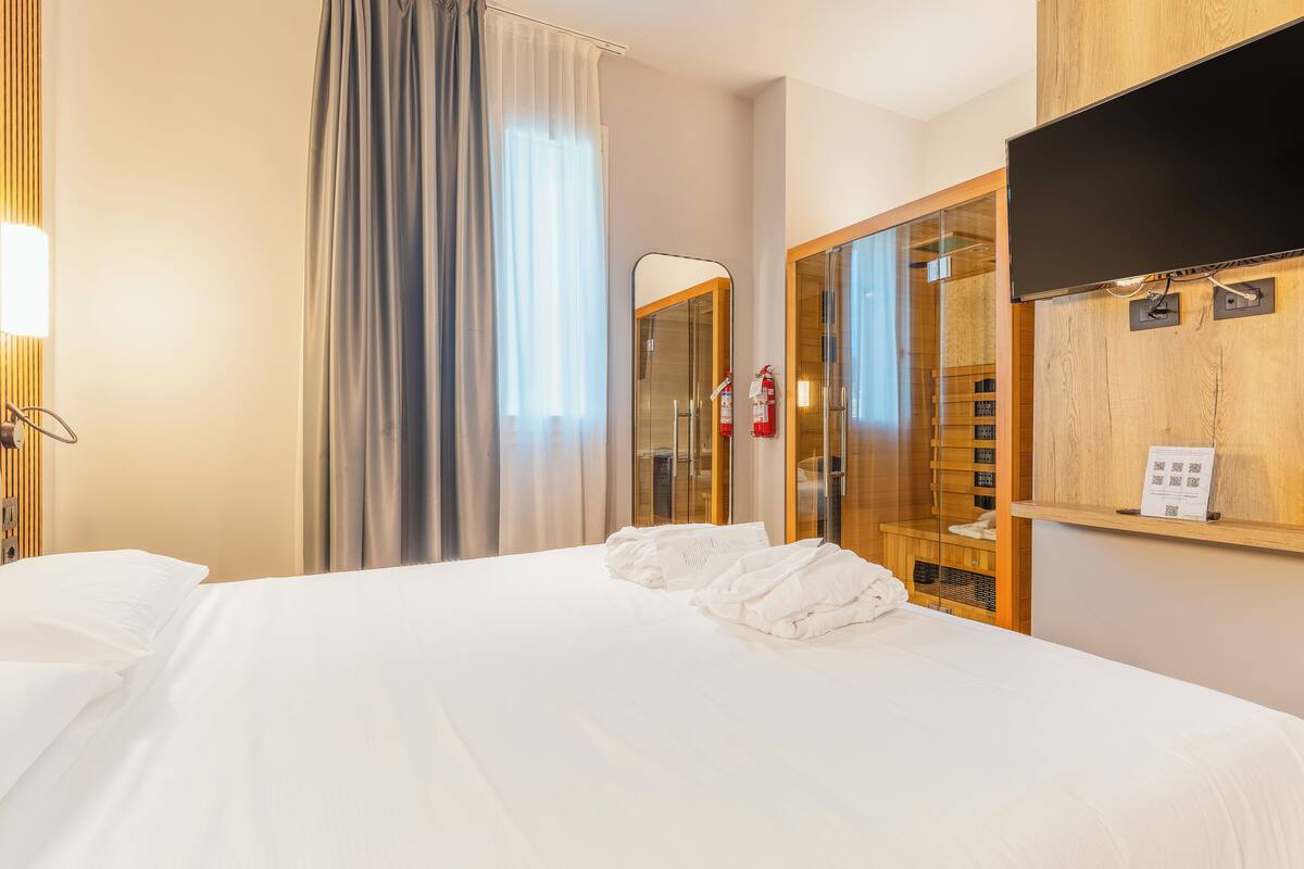 Una habitación de hotel con una cama, un espejo, un televisor y un armario.