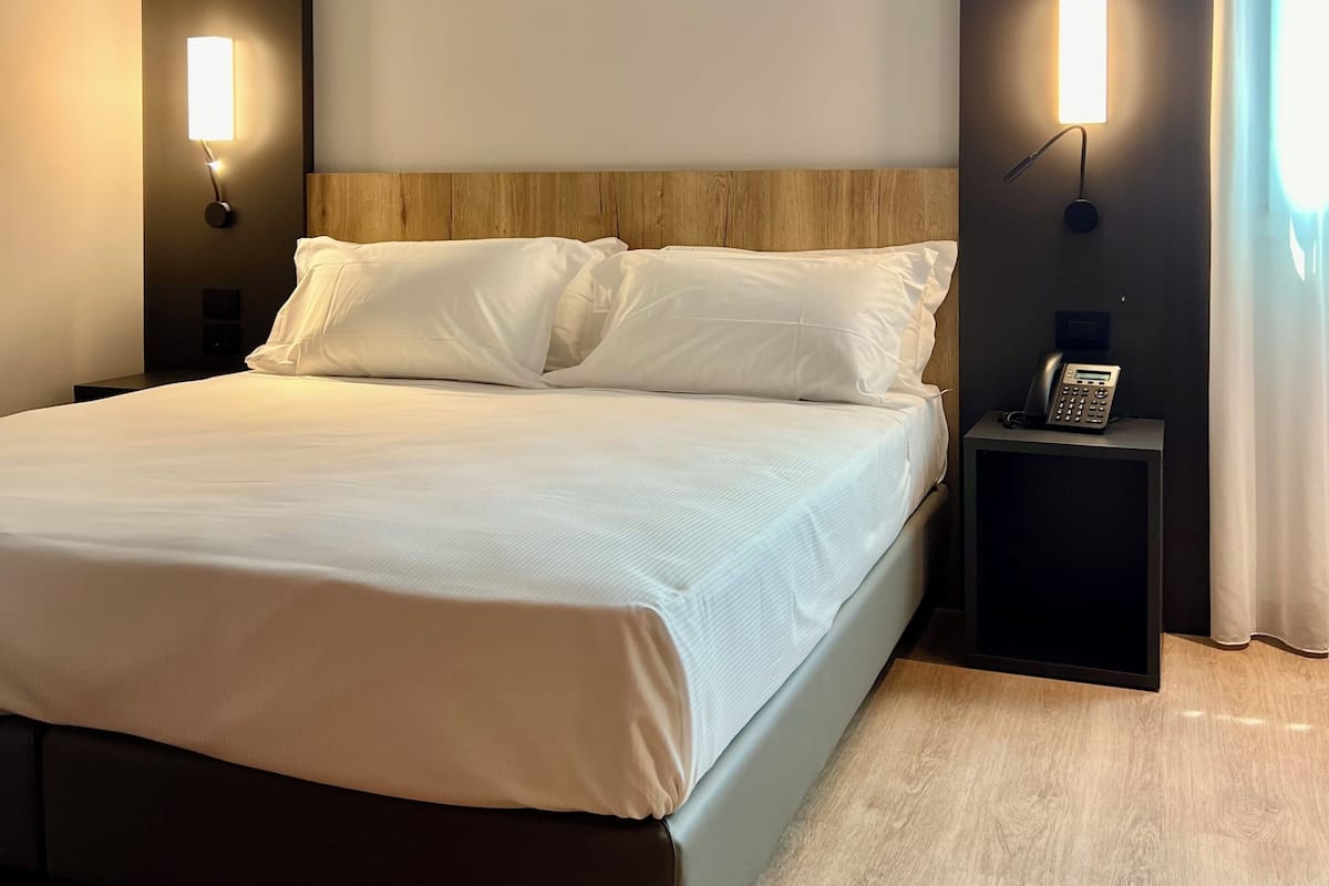 Una cama bien hecha con sábanas blancas, dos mesitas de noche con lámparas de pared y un cabecero de madera.