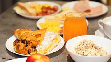 A breakfast setting with croissants, fruit, cereal, and a glass of orange juice on plates.
