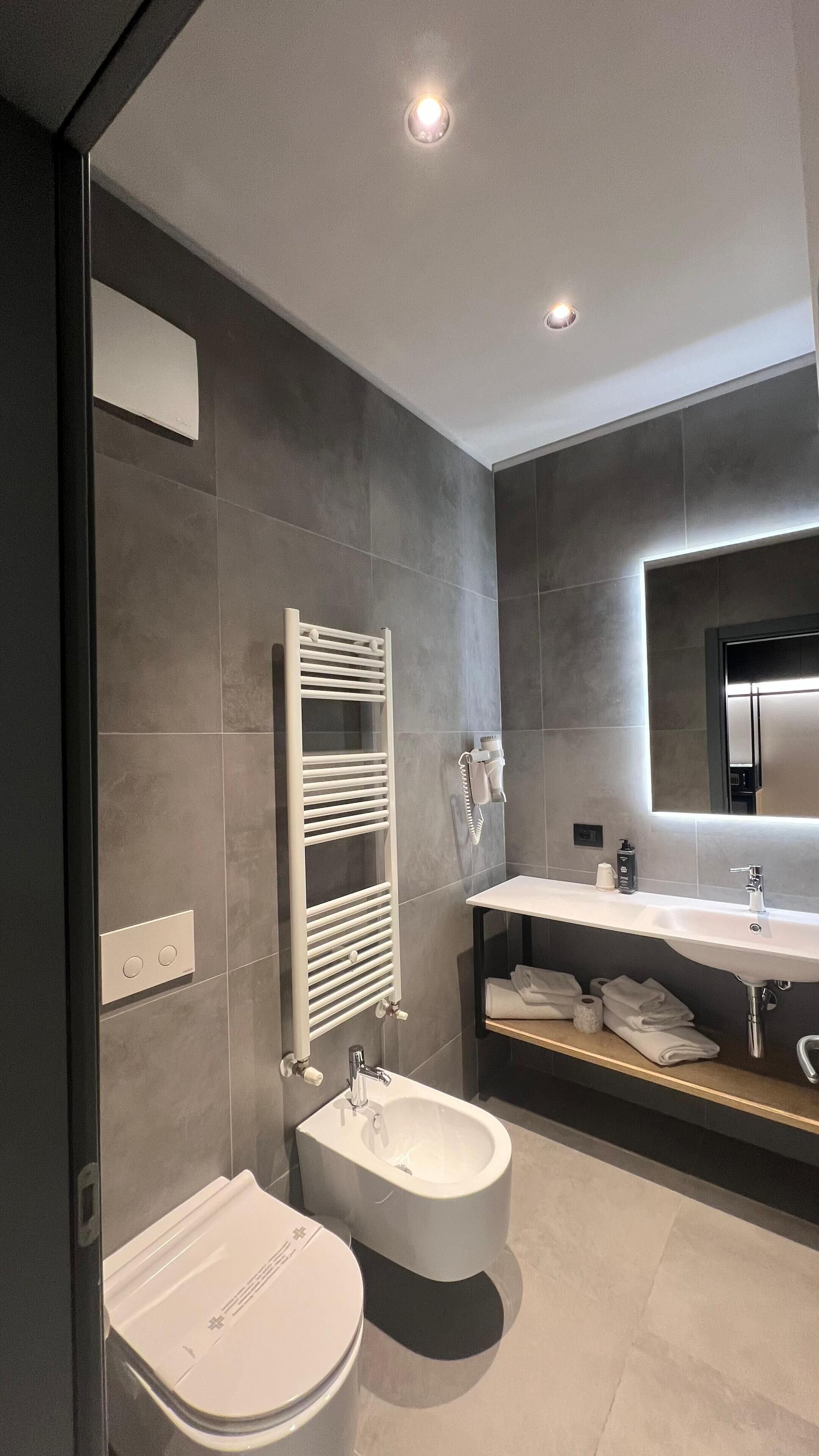 A modern bathroom with a toilet, bidet, towel rack, and a mirror above the sink.