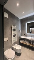 A modern bathroom with a toilet, bidet, towel rack, and a mirror above the sink.