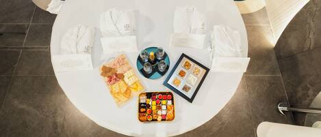 A circular table with towels, snacks, and a tray of assorted items, surrounded by white chairs.