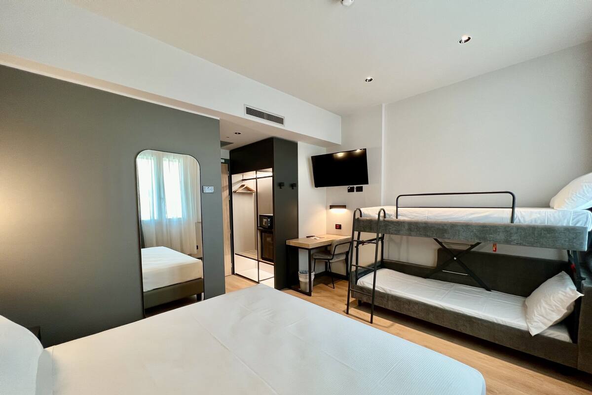 Habitación de hotel pequeña con literas, un escritorio, una silla, un televisor y un vestidor.