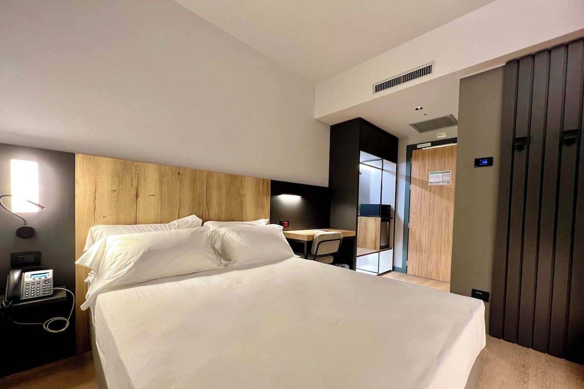 Una habitación de hotel moderna con una cama grande, un escritorio, una silla, un teléfono y un armario.
