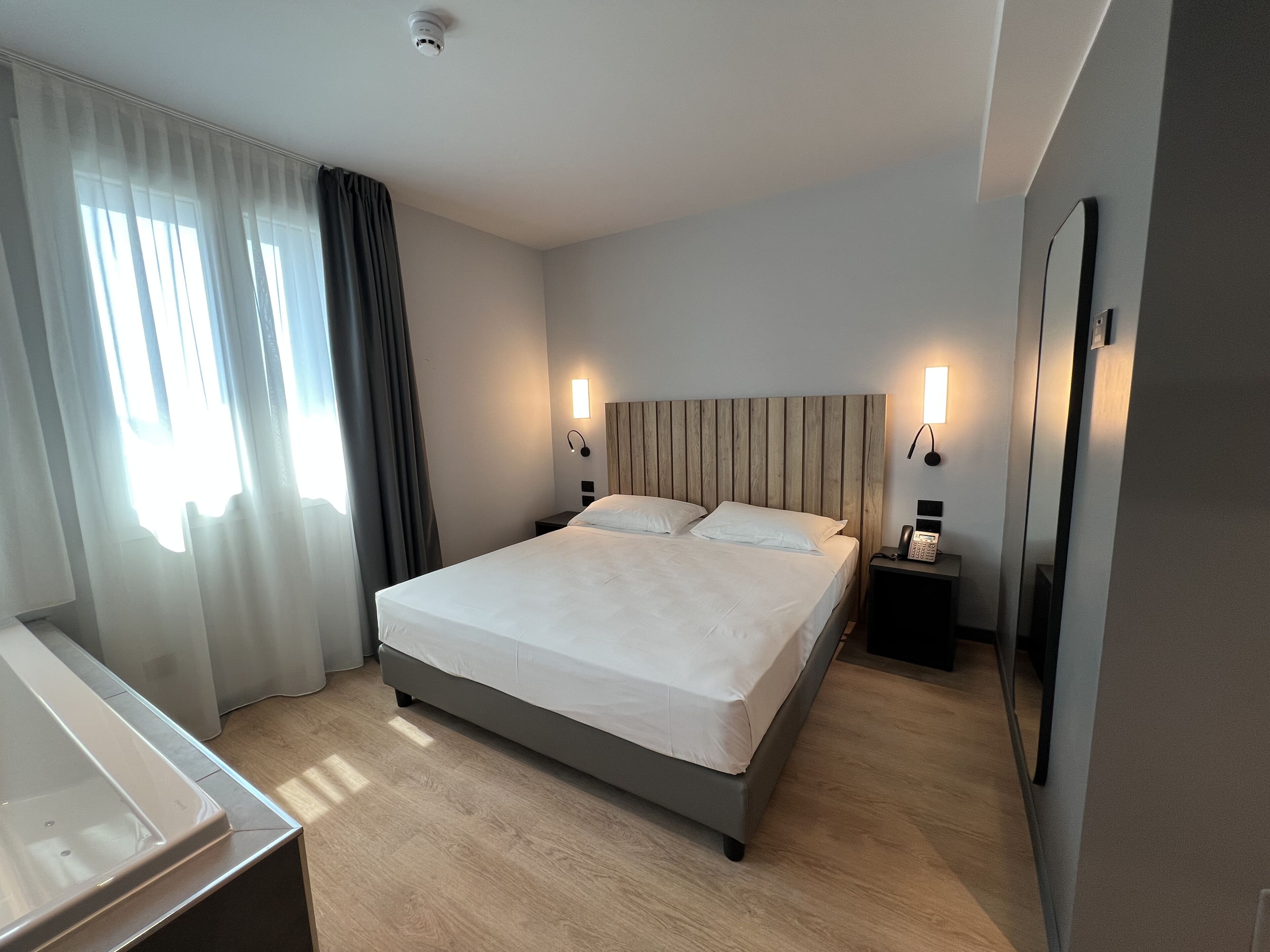Una camera d'albergo con un letto, comodini, una scrivania e uno specchio.