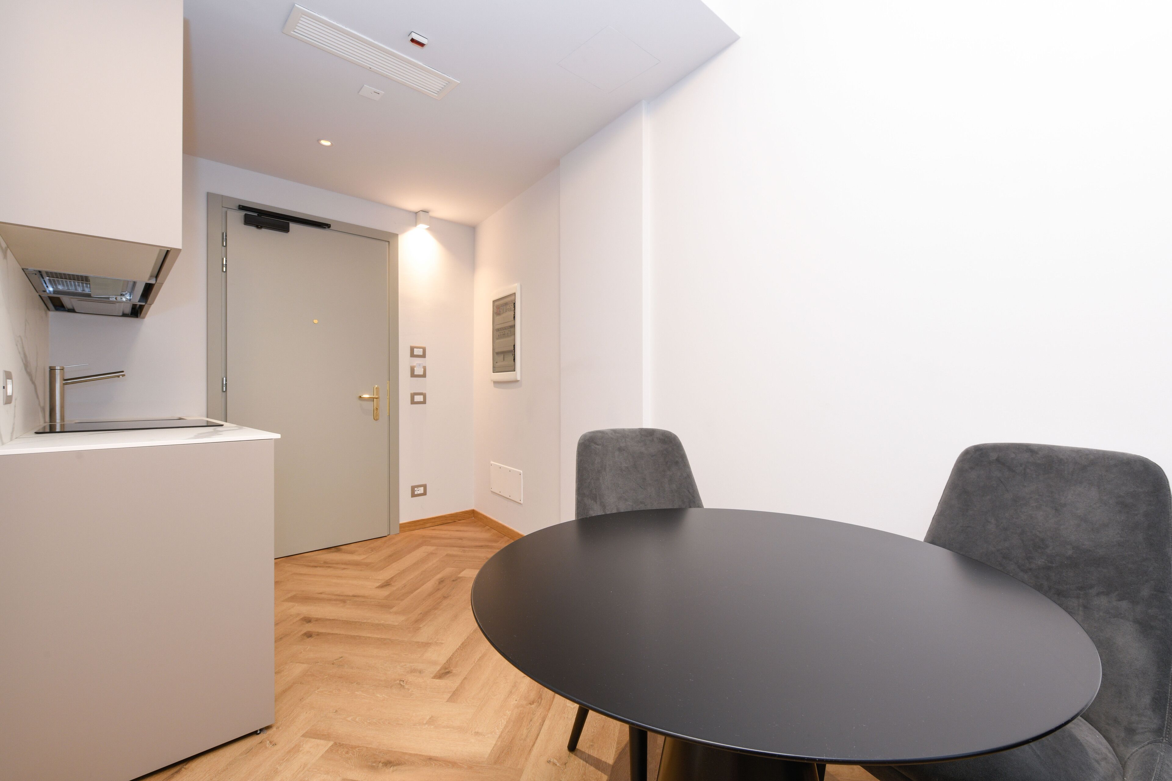A modern room with a round black table, two grey chairs, a white cabinet, and a door leading to another room.
