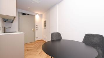 A modern room with a round black table, two grey chairs, a white cabinet, and a door leading to another room.
