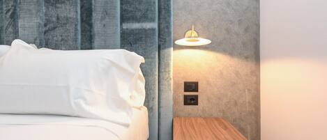 A neatly made bed with white linens, a small wooden nightstand with a lamp, and a textured grey wall.