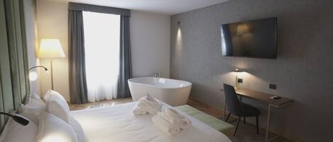 Quarto de hotel com uma cama grande, escrivaninha, televisão de tela plana, banheira e janela com cortinas.