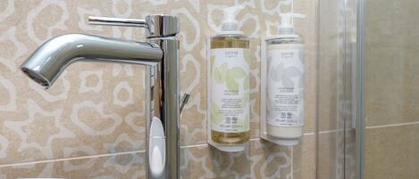 Ein Badezimmer mit modernem Wasserhahn, einer Wand mit gemusterten Fliesen und zwei Flaschen biologischer Handseife.
