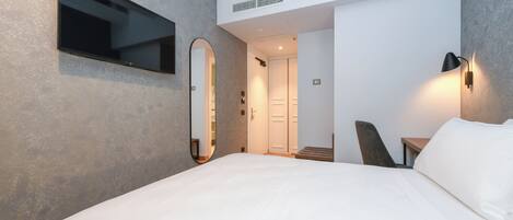 Una habitación de hotel moderna con una cama grande, un televisor de pantalla plana montado en la pared, un escritorio con una silla y un espejo.
