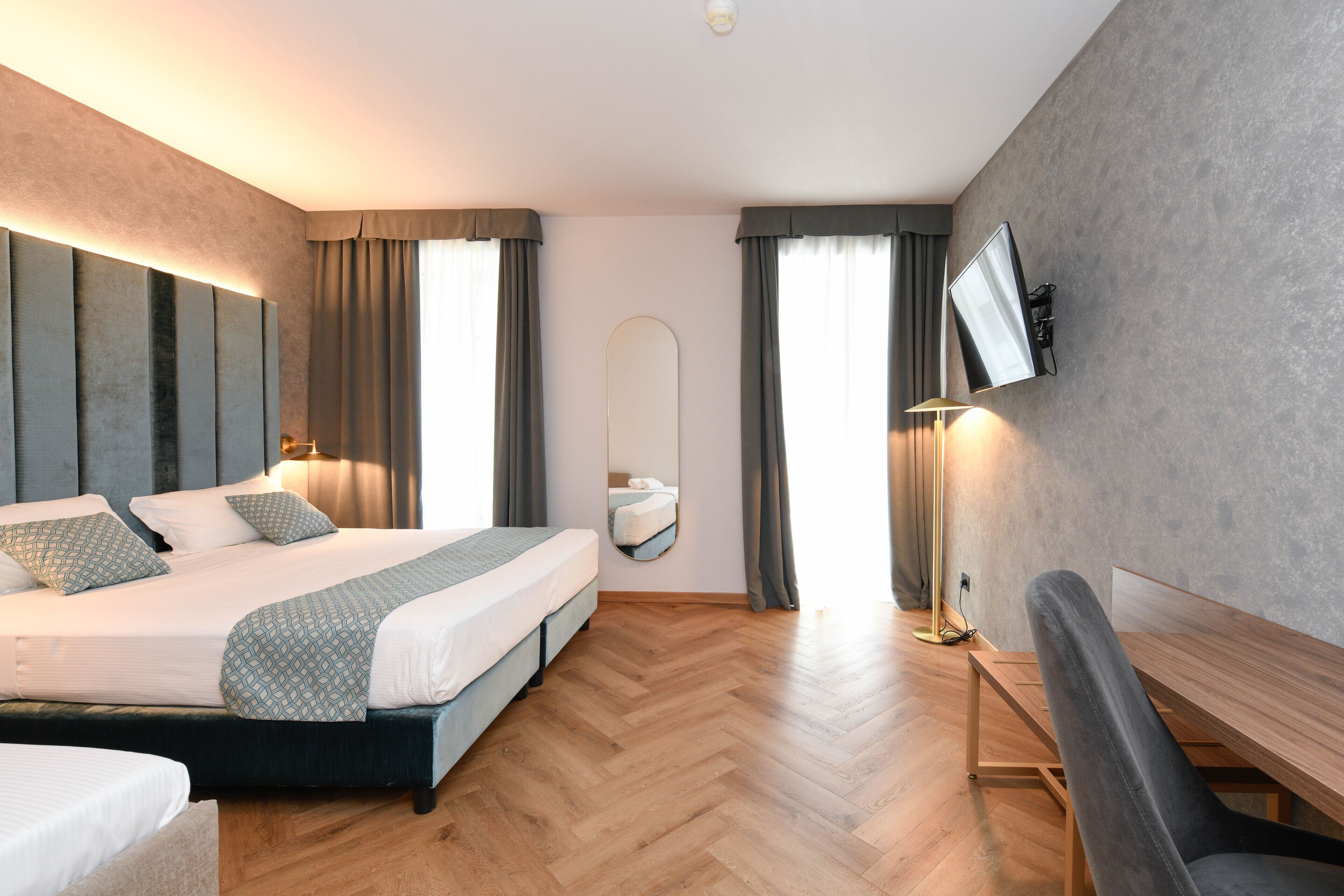 Quarto de hotel moderno com uma cama grande, escrivaninha, televisão de tela plana na parede e um espelho amplo.