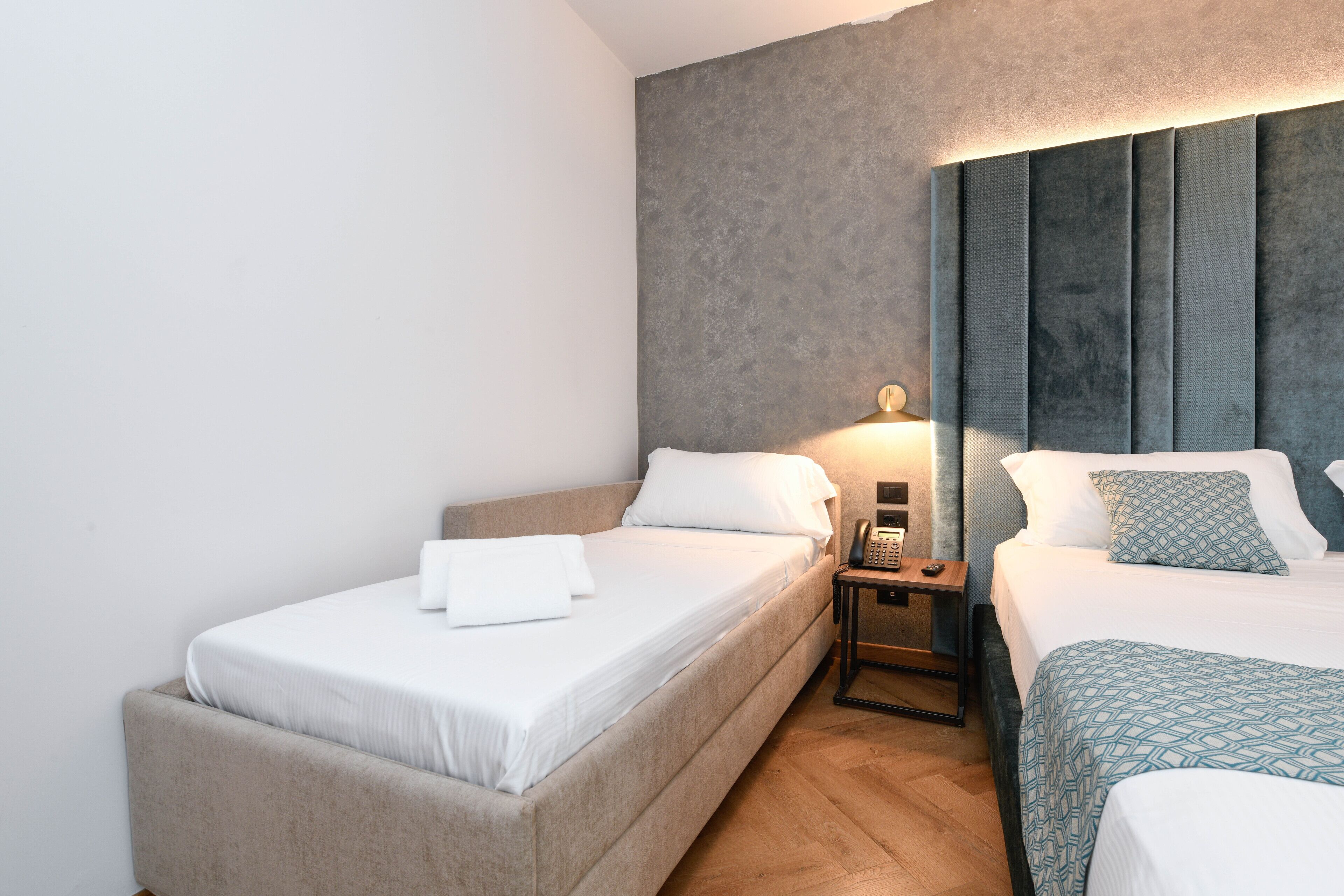 A hotel room with two beds, a nightstand with a phone, and a wall with a textured pattern.