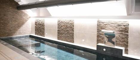 Un área de spa con una piscina larga y estrecha, paredes de piedra y un grifo moderno.