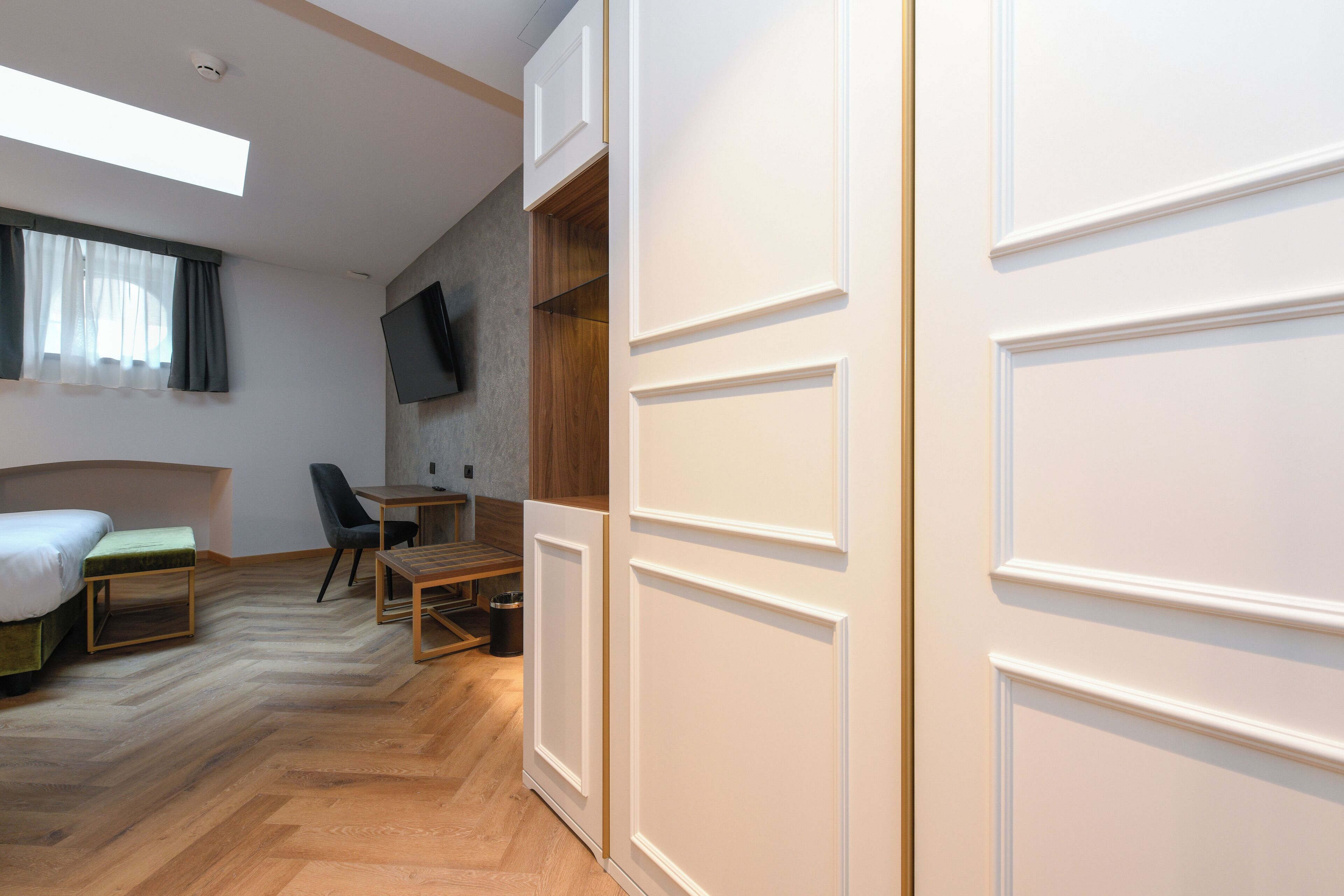 Une chambre d’hôtel moderne avec un plancher en bois, un lit, un bureau, une chaise et un téléviseur fixé au mur.