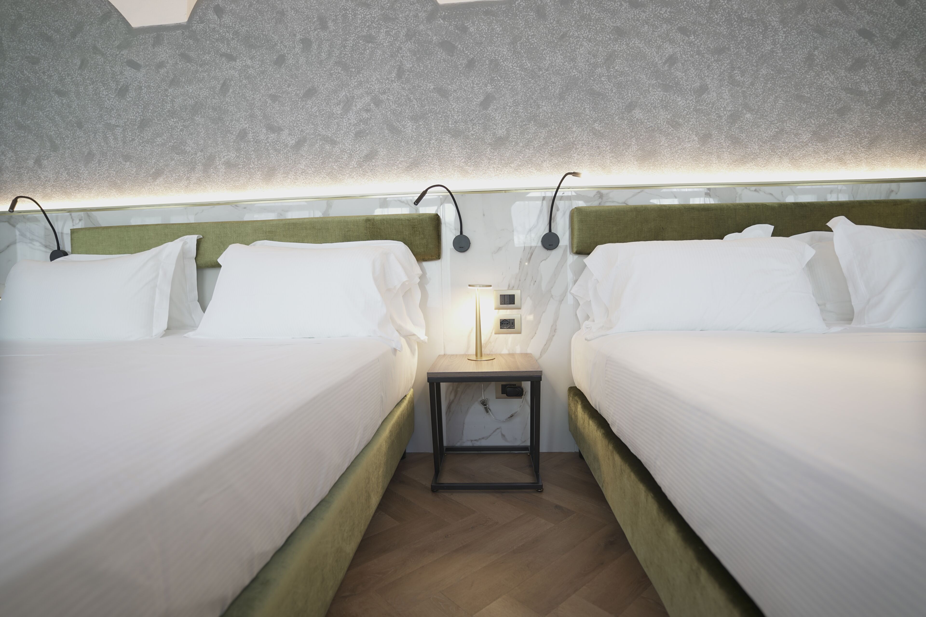 A hotel room with two beds, a nightstand with a lamp, and a patterned ceiling.