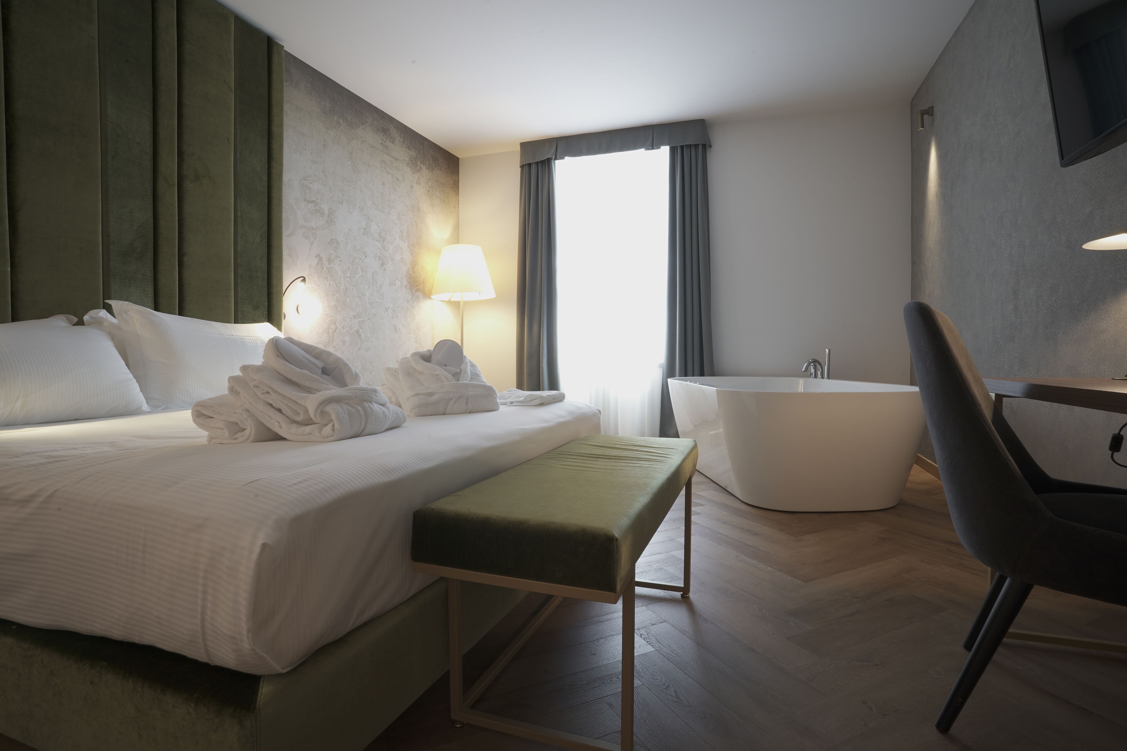 Quarto de hotel moderno com uma cama grande, um banco, uma banheira e uma cadeira.