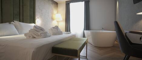 Quarto de hotel moderno com uma cama grande, um banco, uma banheira e uma cadeira.