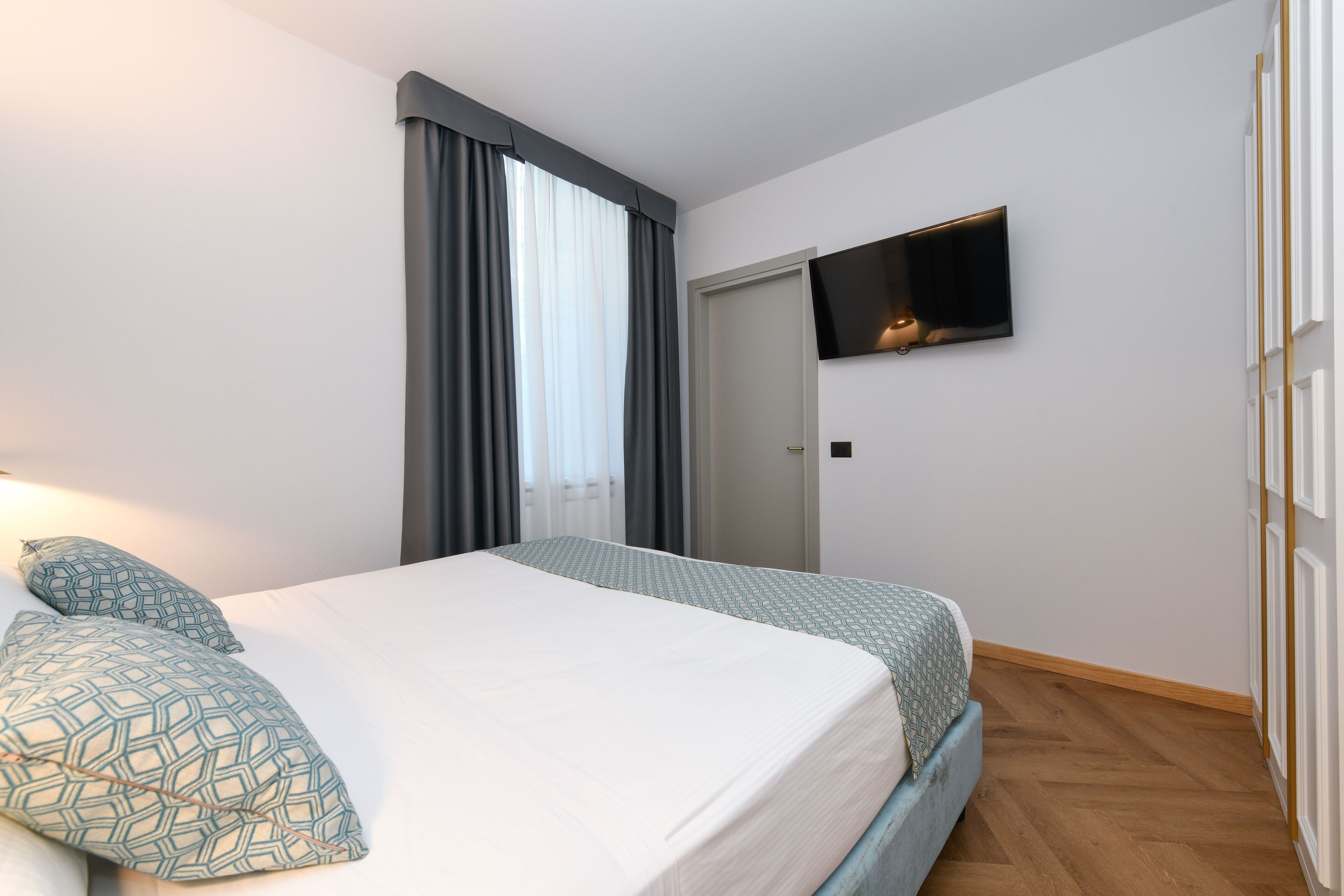 Una habitación de hotel con cama, cortinas, un televisor en la pared y una puerta.