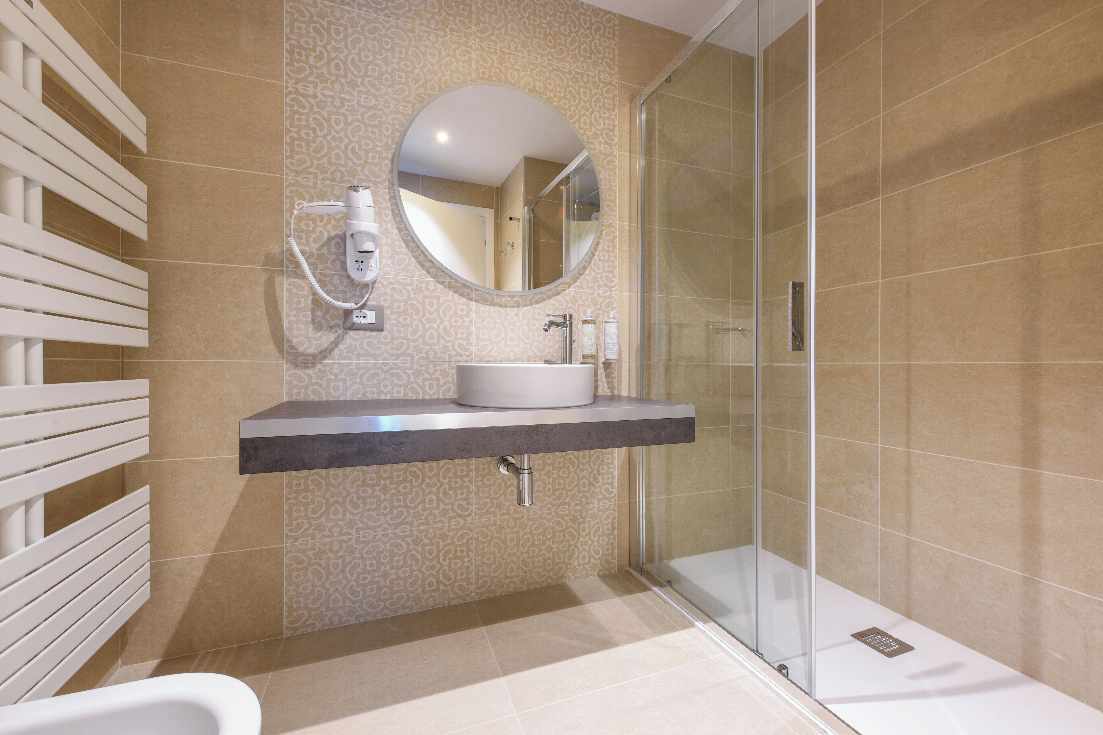 A modern bathroom with a built-in sink, a round mirror, a handheld showerhead, and a glass-enclosed shower.
