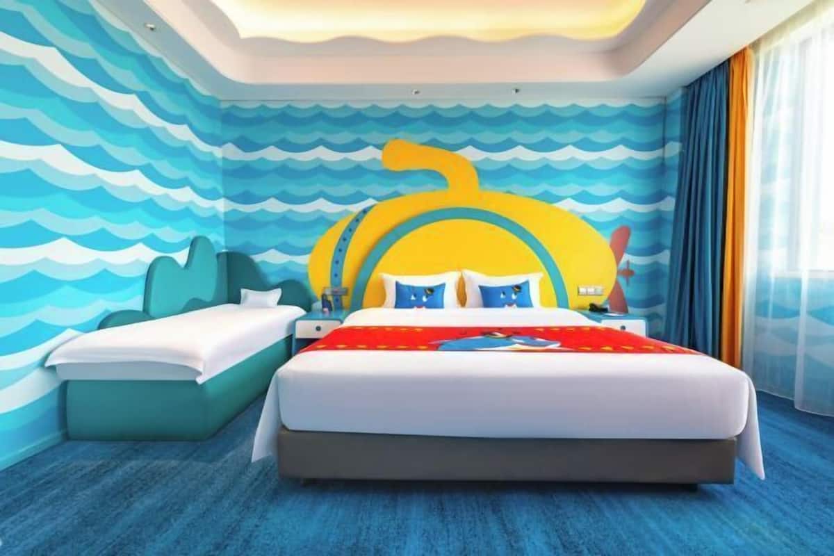 Una habitación de hotel con una cama, una mesita de noche, un mural en la pared y una ventana con cortinas.