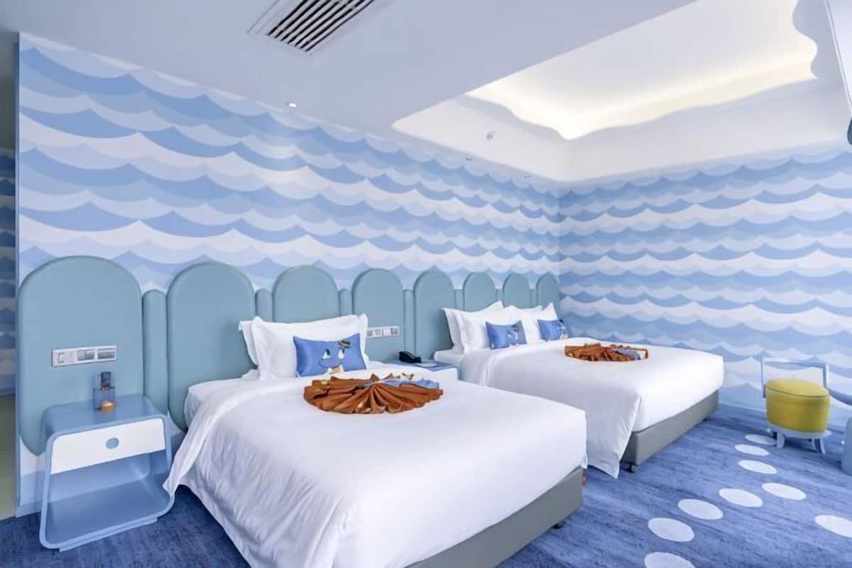 Habitación de hotel con dos camas, una mesita de noche, una pequeña mesa y una pared con diseño de olas.