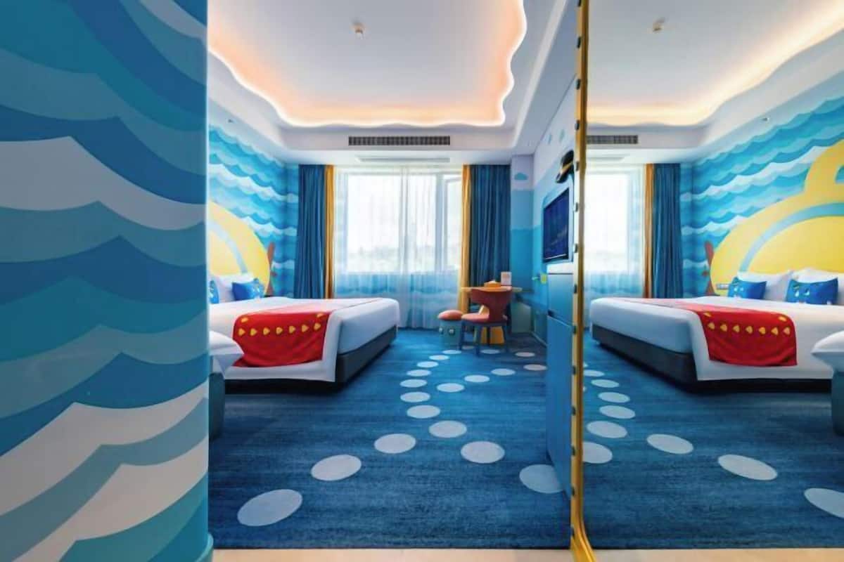Habitación de hotel con dos camas, una alfombra azul con lunares y una pared con motivos de olas.