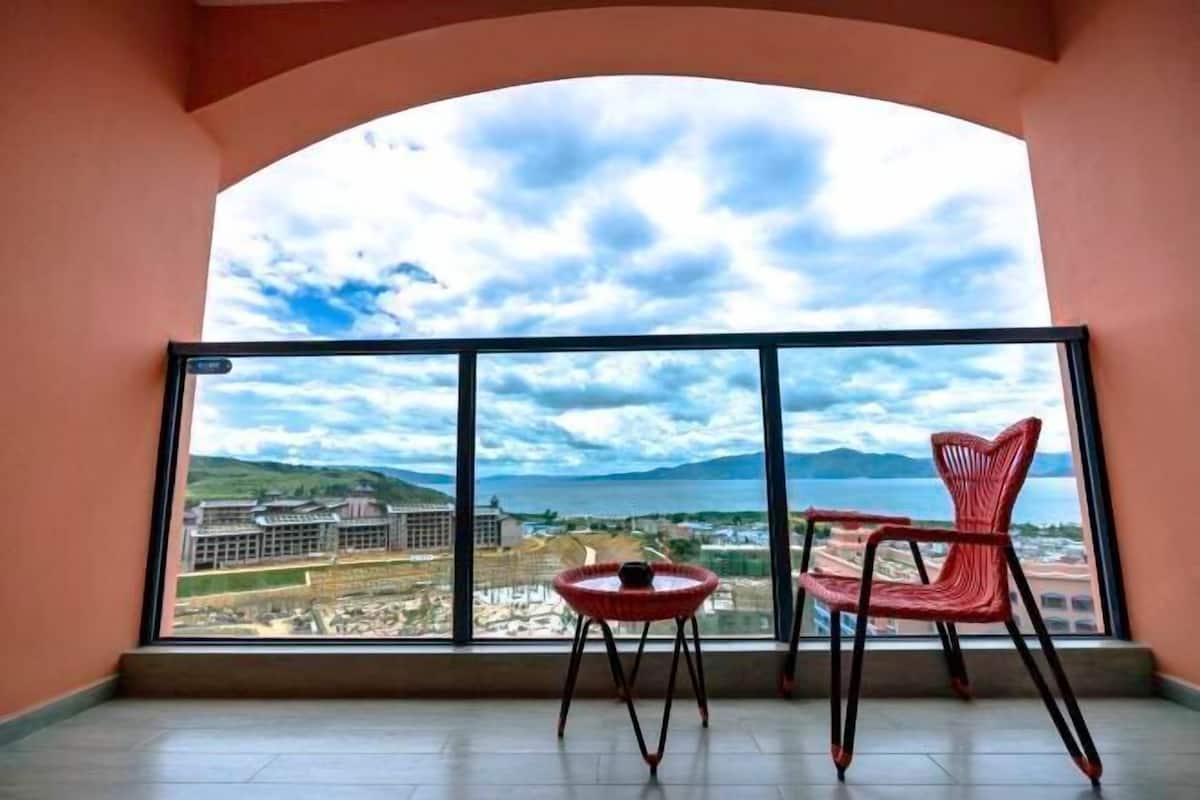 Un balcón con vistas a una ciudad costera, una silla roja y una pequeña mesa.