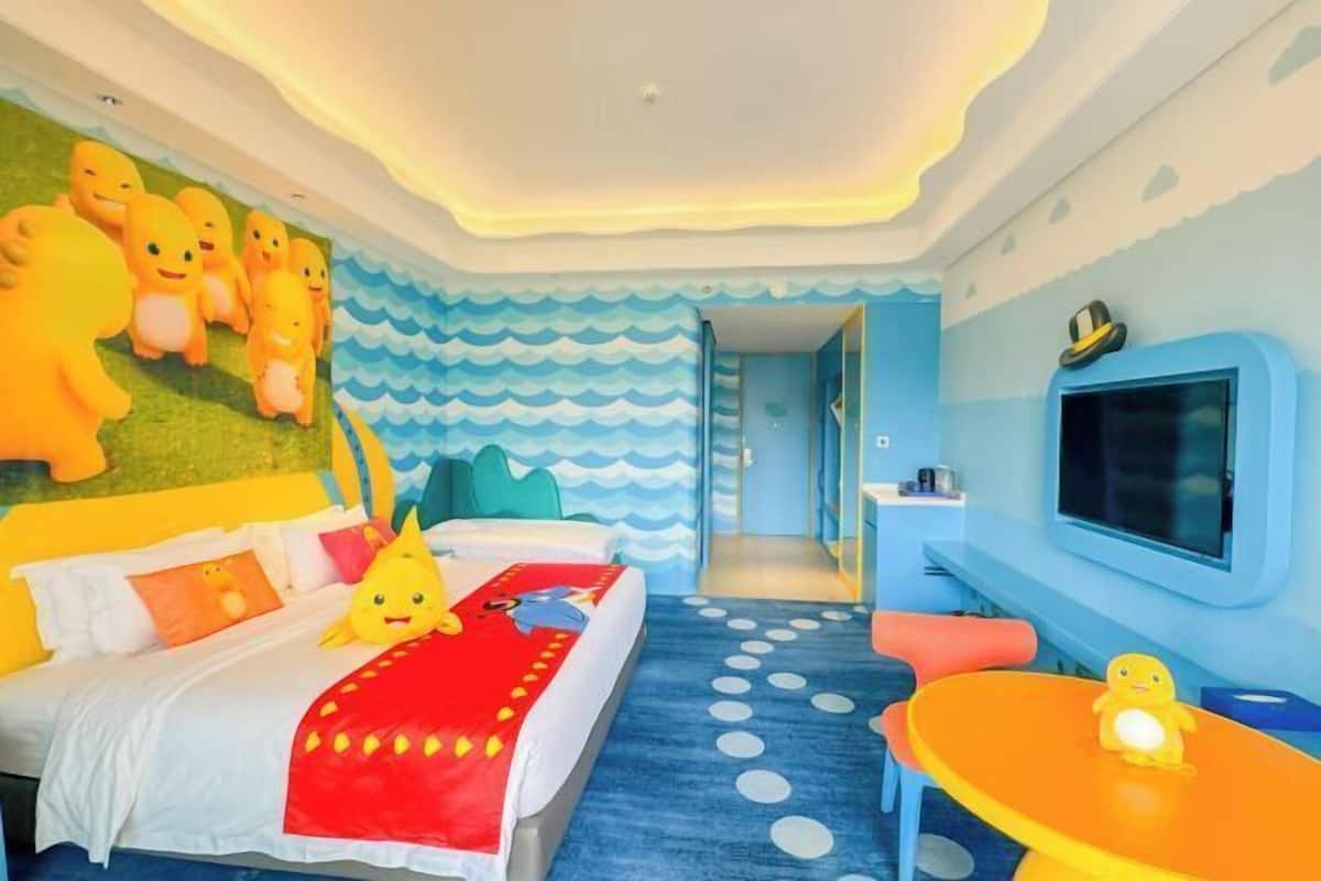 Una habitación infantil con cama, una mesita, televisor y adornos en la pared.