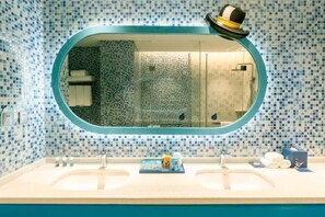 Un baño con un espejo ovalado grande, dos lavamanos y un salpicadero de azulejos.