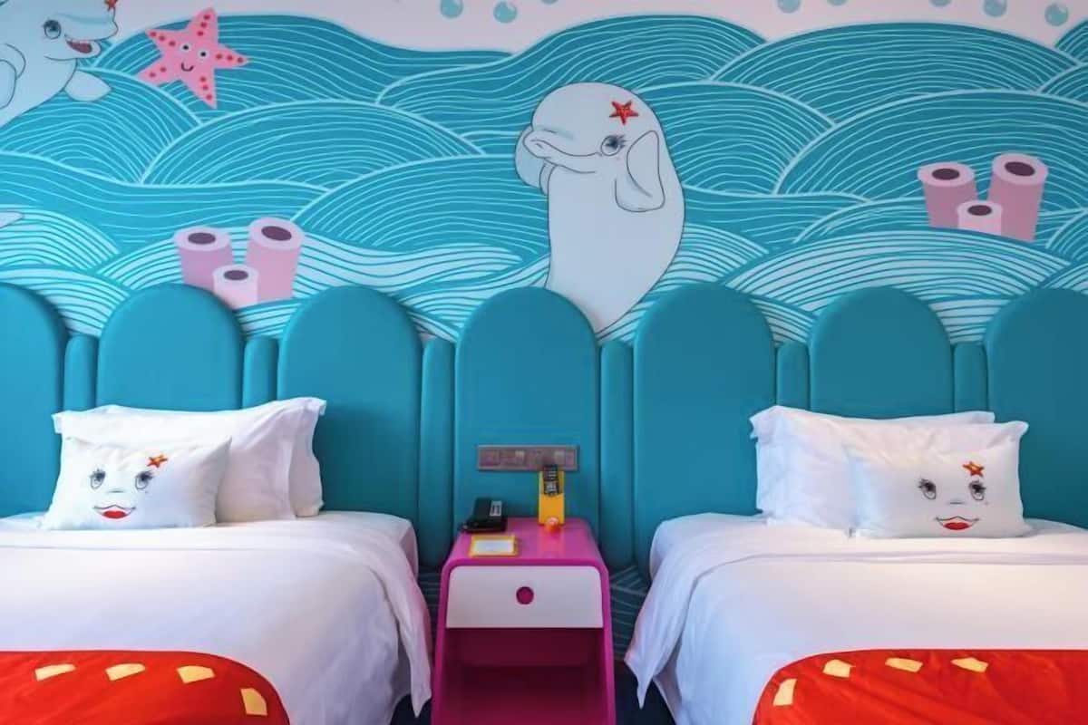 Una habitación con dos camas, una mesita de noche y un mural en la pared.