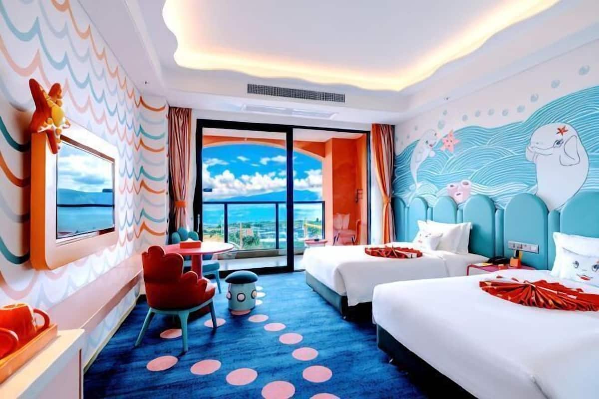 Habitación de hotel con dos camas, una mesa de comedor, una silla y vista al mar, además de un mural en la pared.