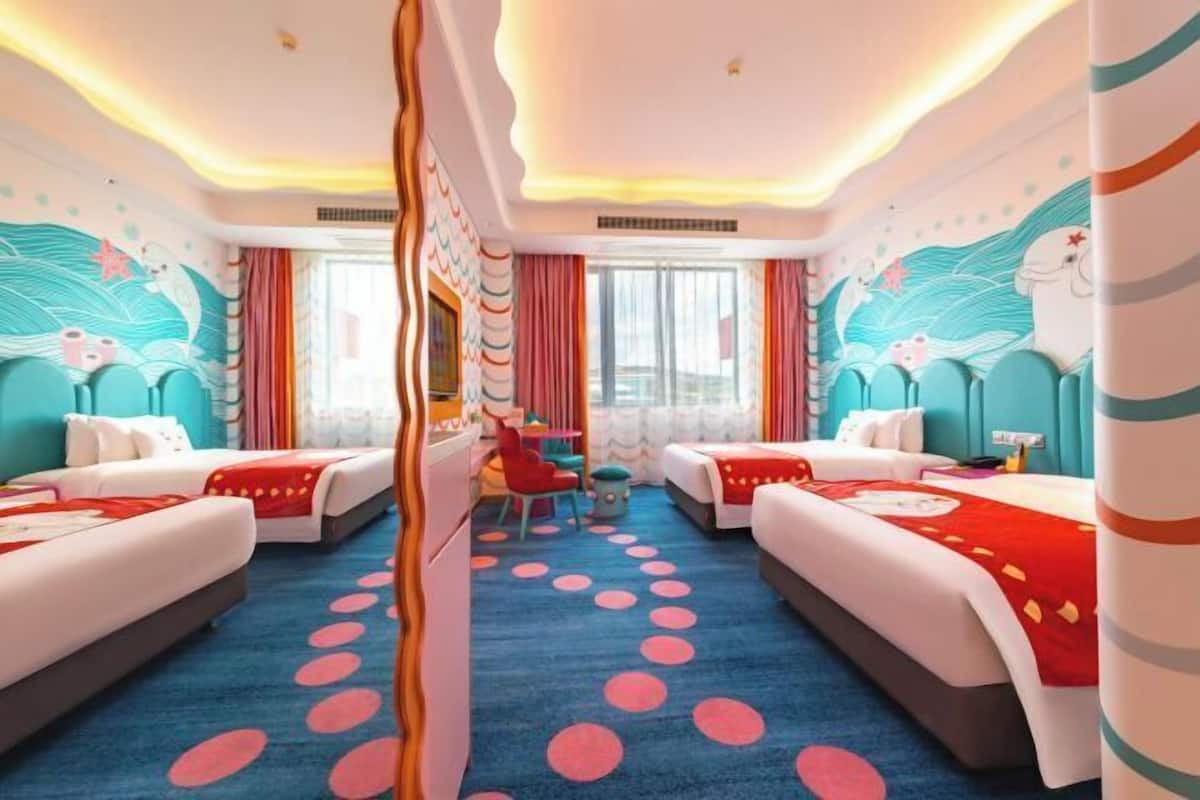 Una habitación de hotel con dos camas, una mesita pequeña, una silla y una alfombra colorida.