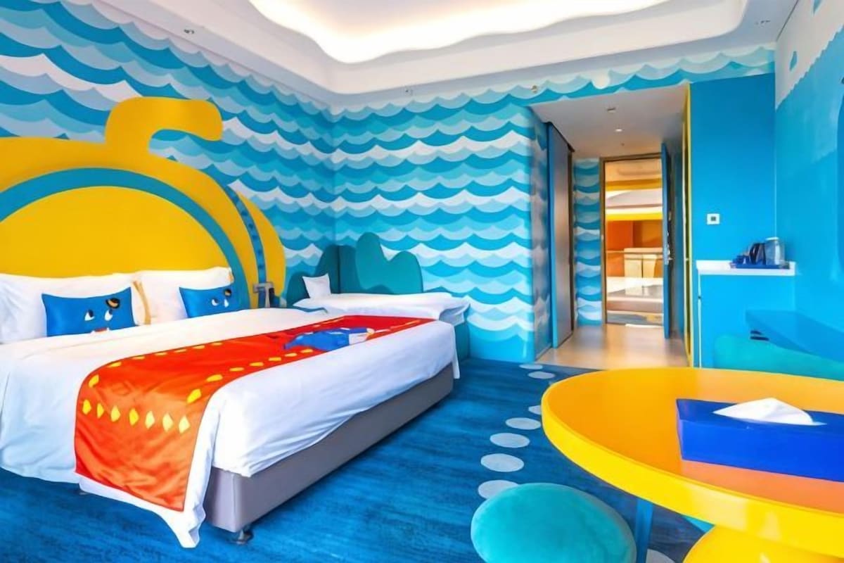 A hotel room with a large bed, a small table, and a view of the hallway.