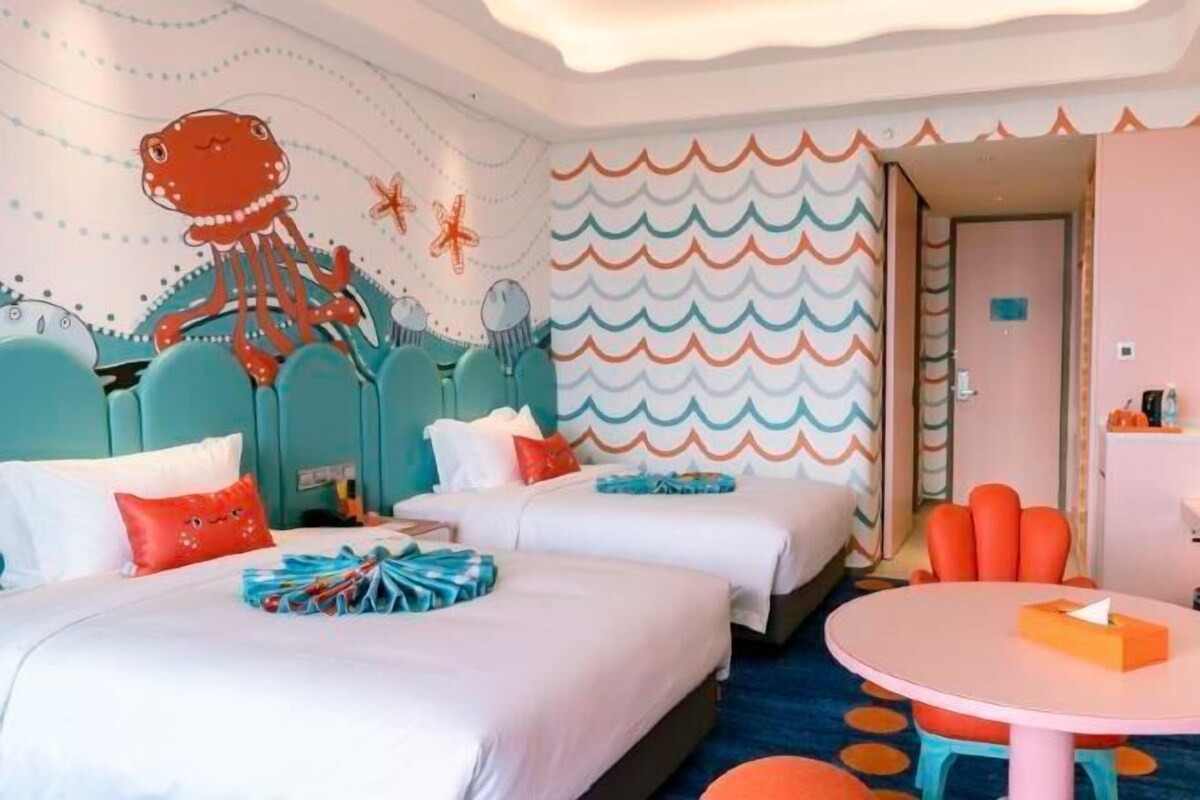 Una habitación de hotel con dos camas, una mesa redonda y una pared con un diseño de olas.