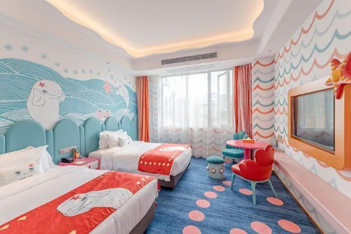 Habitación de hotel con dos camas, televisión, una mesita y ventana con cortinas.